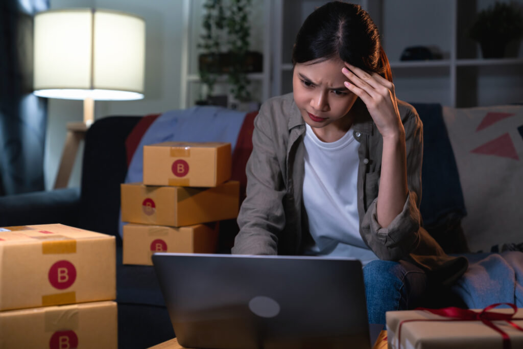 Why Growing Businesses Suddenly Face Delivery Complaints startup small business concept, young woman owner hands touch on the forehead have a headache because of stress, and checking online order on digital laptop with packing on the box at home office.