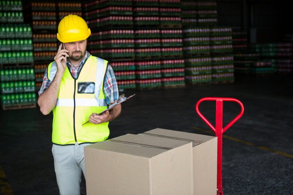 Why Organized Logistics Systems Are Critical for Smooth Operations young male worker holding clipboard while talking on phone in factory