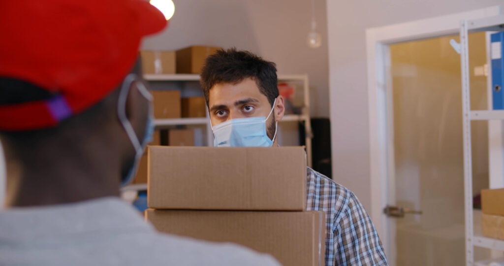 view over shoulder of courier in mask give package to distribution warehouse worker