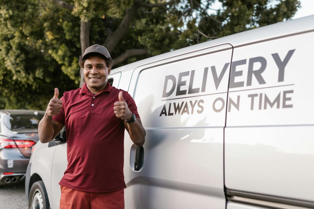 How Fast Delivery Improves Customer Satisfaction Happy deliveryman in maroon shirt giving thumbs up by delivery van outdoors.